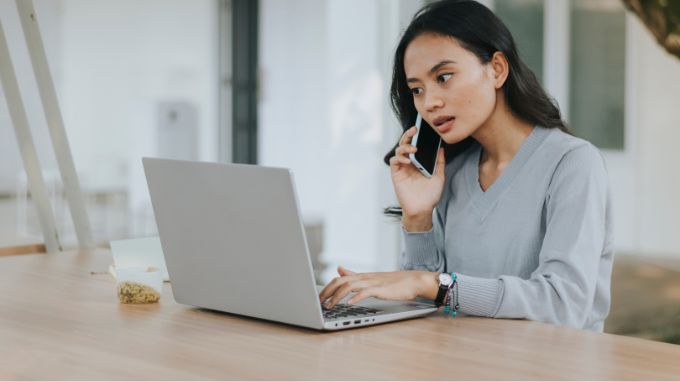 a woman talking on a cell phone while using a laptop